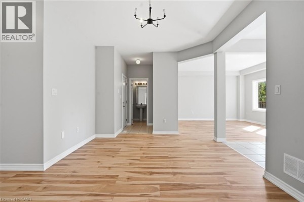 Open-concept living and dining area with wood floors, beige furniture, and a crib near a window. - 125 Tumblewood Place, Welland