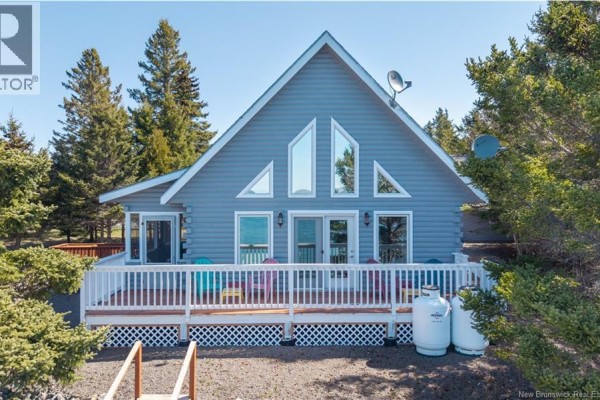 Wooden ramp leading to a white deck on a grey A-frame house surrounded by trees. - 1250 Route 172, L Etete
