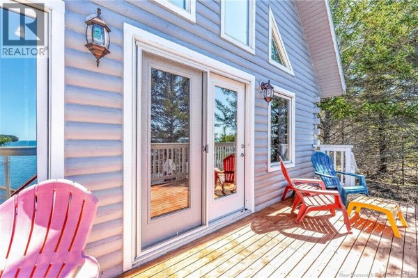 Wooden deck with white railing and colorful chairs overlooking the ocean on a sunny day. - 1250 Route 172, L Etete