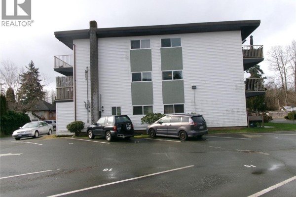 Close-up of the building's side with parking area and balconies, featuring a cloudy backdrop. - 1252 9th St, Courtenay