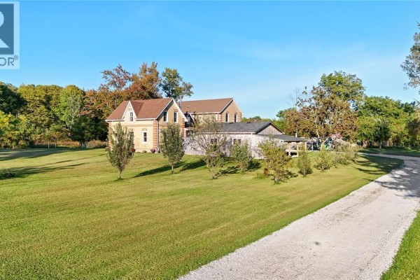 Side view of a yellow brick house with attached garage, driveway, and mature trees on a sunny day. - 1252 Downie Road, Dawn Euphemia