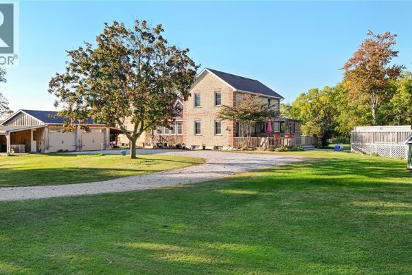 Rear exterior of a yellow brick house with a wooden deck, attached garages, and detached shed. - 1252 Downie Road, Dawn Euphemia