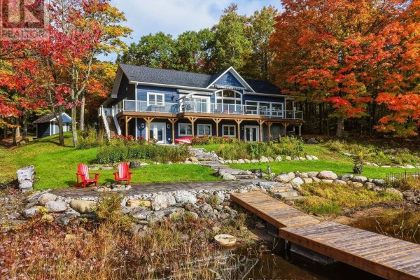 A blue residential house with a large deck and steps leading to a dock on the water. - 1252 Winders Bay Road, Lake Of Bays