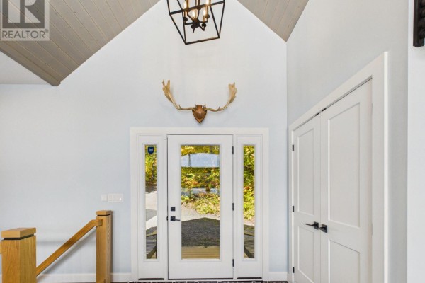 Foyer with vaulted ceiling, glass double doors, moose antlers mounted above, and a staircase railing. - 1252 Winders Bay Road, Lake Of Bays