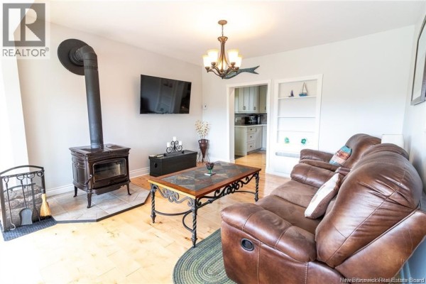 Cozy living room with a wood stove, TV, and coffee table on hardwood flooring - 1253 Rte 772, Cummings Cove