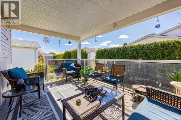 Covered outdoor patio with wicker furniture, glass railing, and an outdoor rug. - 1255 Raymer Avenue Unit# 493, Kelowna