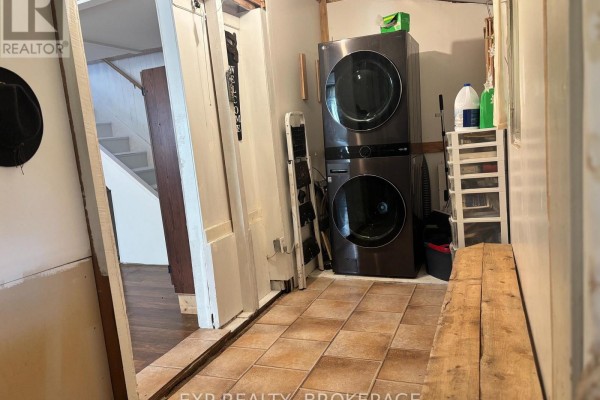 Utility room with stacked washer and dryer, tile floor, and wooden bench. - 1256 Elm Tree Road, Frontenac