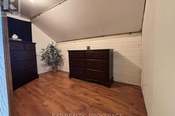 Attic room with sloped ceiling, wood plank walls, two dark wood dressers, and wood flooring. - 1256 Elm Tree Road, Frontenac