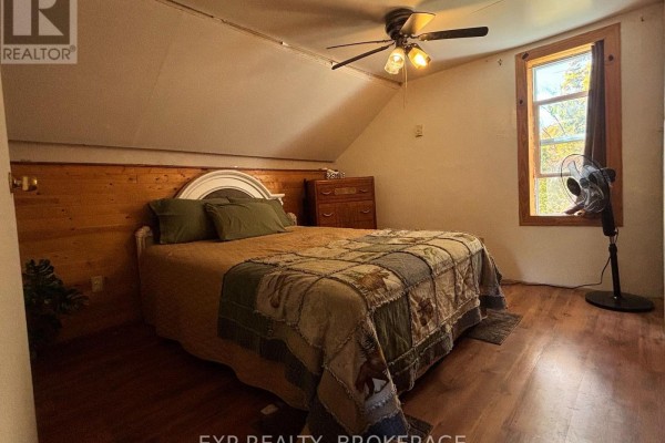 Bedroom with a queen-size bed, wood flooring, sloped ceiling, and a window with fall foliage view. - 1256 Elm Tree Road, Frontenac