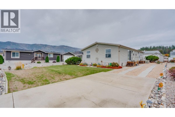 View of mobile homes in a community with a paved driveway and grass lawn. - 12560 Westside Road Unit# 15, Vernon