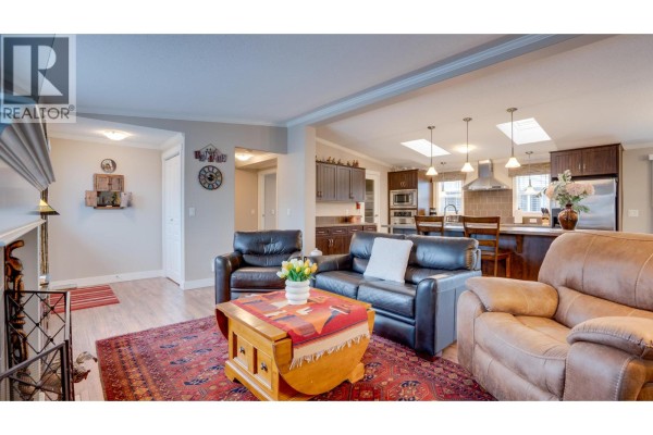 Living room with leather couches and a wooden coffee table, opening to a kitchen and dining area. - 12560 Westside Road Unit# 15, Vernon