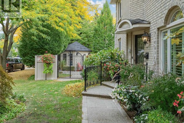 Pathway leading to the entrance of a beige brick house with a fenced garden and small shed. - 1259 Nathaniel Crescent, Burlington