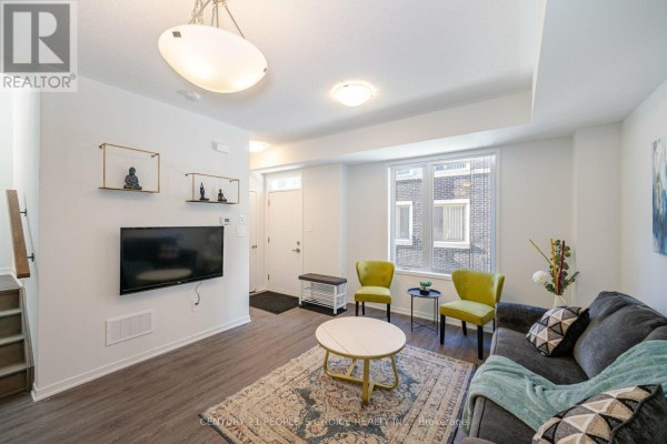 Living room with dark grey sofa, patterned rug, yellow accent chairs, and a television on the wall. - 126 - 30 Almond Blossom Mews, Vaughan