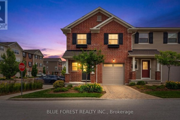 Red brick townhouse with beige siding at dusk, interior lights on, driveway lit. - 126 - 3025 Singleton Avenue, London South