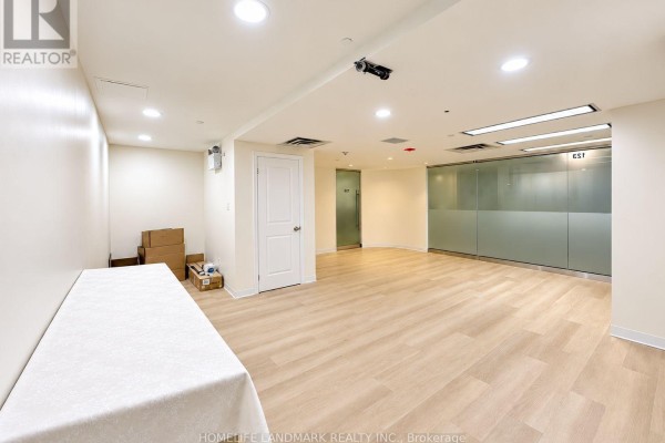 Empty commercial space with light wood floors, white walls, and a table covered with a white cloth. - 126 - 7155 Woodbine Avenue, Markham