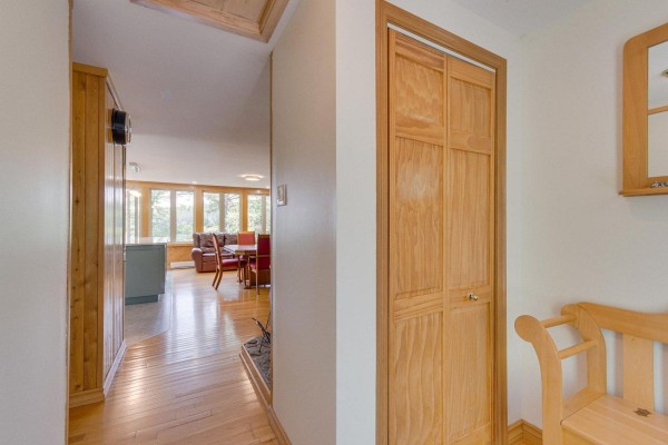 Hallway leading to a living and dining area with light wood floors and large windows overlooking a wooded landscape. - 126-129 Ch. Richard, Bouchette