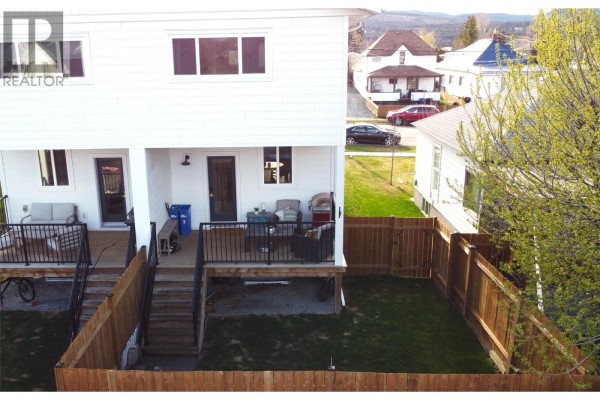 Rear exterior of a white duplex showing two separate fenced backyards with decks and outdoor furniture. - 126 13th Avenue S Unit# A & C, Cranbrook