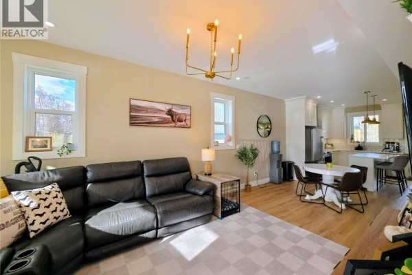 Living room with a black leather sectional sofa, checkered rug, dining area, and kitchen with white cabinets. - 126 13th Avenue S Unit# A & C, Cranbrook