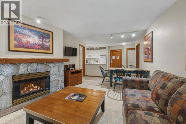 Living room with a stone fireplace, floral couch, purple armchair, and a sliding glass door. - 126 4800 Spearhead Drive, Whistler