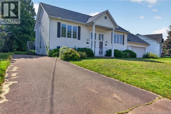 Side exterior view of the white house with a paved driveway and green lawn. - 126 Bahama Street, Dieppe