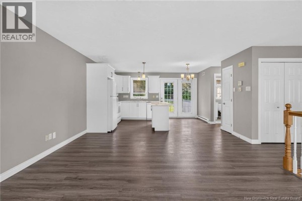 Open-concept living area with a white kitchen, island, and double doors to the outside. - 126 Bahama Street, Dieppe