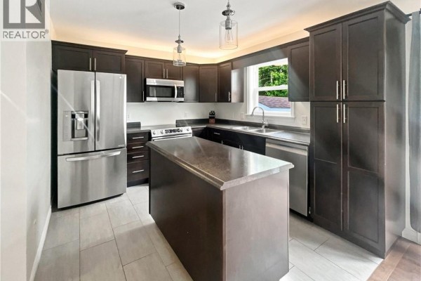 Modern kitchen with dark wood cabinets, stainless steel appliances, and a grey island with a stone countertop. - 126 Chianti Street, Dieppe