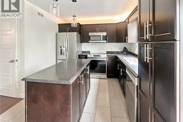 Kitchen with dark wood cabinetry, stainless steel appliances, and a grey island, viewed from the side. - 126 Chianti Street, Dieppe