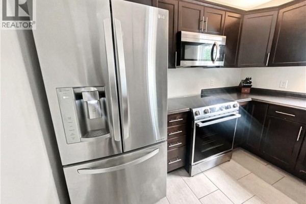 Close-up of stainless steel refrigerator and stove in a kitchen with dark wood cabinets. - 126 Chianti Street, Dieppe