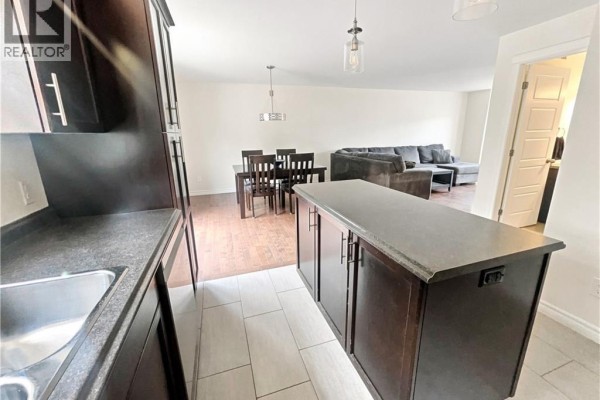 View from the kitchen island into an open-concept living and dining area with a sectional sofa and dining table. - 126 Chianti Street, Dieppe