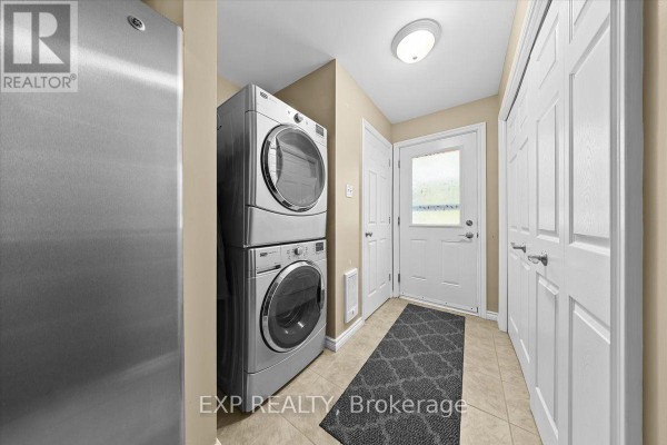 Laundry room with stacked silver washer and dryer, tan walls, tiled floor, and white doors. - 126 Gardiner Shore Road, Beckwith