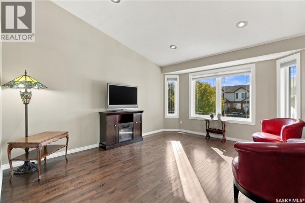 Living room with hardwood floors, taupe walls, and a large bay window overlooking the street. - 126 Lamarsh Road, Saskatoon