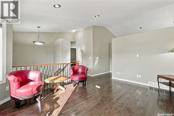 Living room with hardwood floors, taupe walls, a railing, and a view of hallways. - 126 Lamarsh Road, Saskatoon