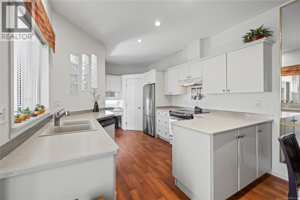 White kitchen with stainless steel appliances, granite countertops, wood floors, and a desk area. - 126 Ocean Walk Dr, Nanaimo