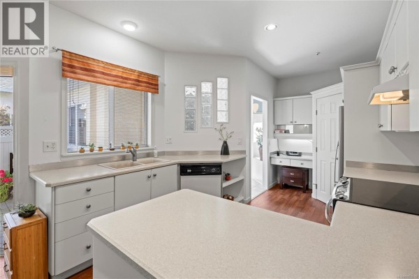 Kitchen view showing sink, dishwasher, ample counter space, white cabinets, and a desk. - 126 Ocean Walk Dr, Nanaimo
