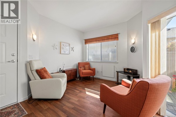 Living area with two orange armchairs, a reclining chair, wood floors, and sliding glass door. - 126 Ocean Walk Dr, Nanaimo
