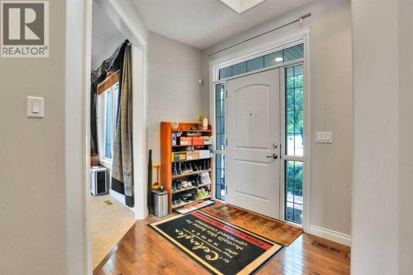 Foyer entrance with double doors, hardwood floors, and a shoe rack. - 126 Panatella Crescent Nw, Calgary