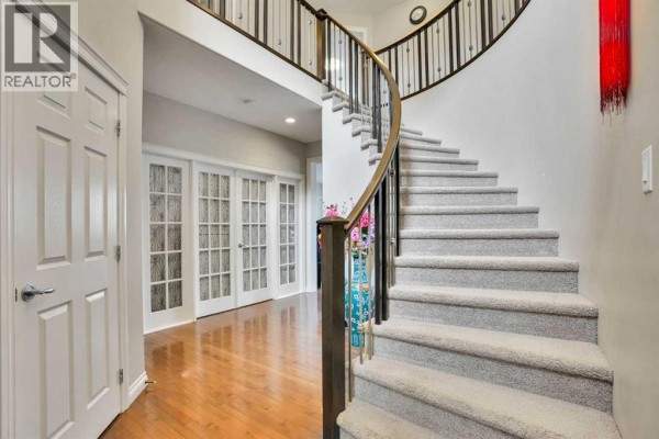 Grand staircase with carpeted steps and a dark wood banister in the foyer. - 126 Panatella Crescent Nw, Calgary