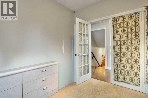 Bedroom with French doors leading to a hallway and a dresser against the wall. - 126 Panatella Crescent Nw, Calgary