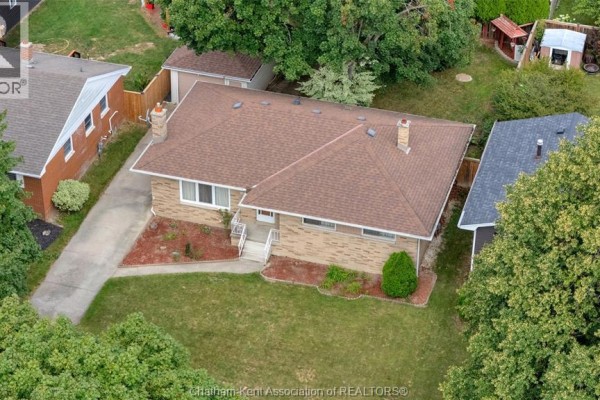 Aerial view showing a brick bungalow with a driveway, garage, and mature trees. - 126 Partridge Crescent, Chatham