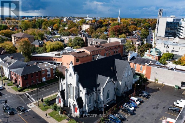 Aerial view of stone church building on corner lot with parking lot and cityscape. - 126 Wellington Street, Kingston