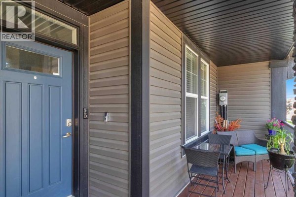 Covered porch area with a blue front door, small table, chairs, and seating. - 126 Williamstown Park Nw, Airdrie