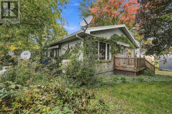 Side view of the house showing brick siding, overgrown vegetation, and satellite dishes. - 12615 County 28 Road, South Dundas