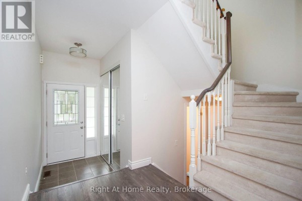 Interior entryway with a white front door, tiled floor, and a carpeted staircase. - 1263 Gyatt Crescent, Oshawa