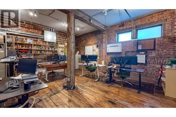 Office space with adjustable desks, computers, exposed brick walls, and wooden floors. - 1264 Ellis Street Unit# B, Kelowna