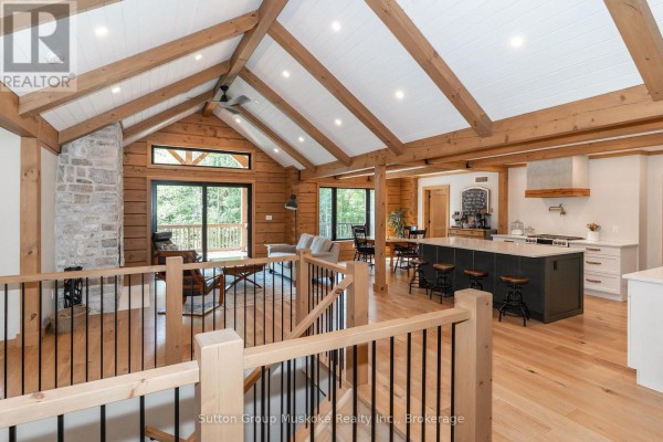 Open concept living area with vaulted wood beam ceiling, stone fireplace, kitchen island, and hardwood floors. - 1265 Britannia Road, Huntsville