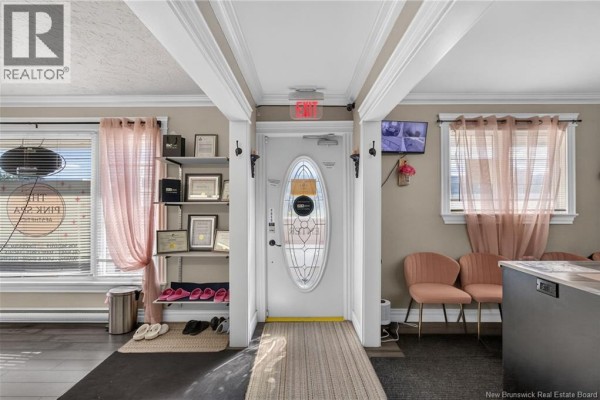 Interior entrance area with a white door, shelves displaying certificates, pink chairs, and large windows with pink curtains. - 1265 Mountain Road, Moncton