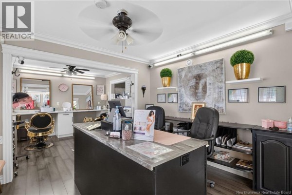 Reception area with a black counter, chairs, artwork, and an open doorway revealing a salon area with styling chairs. - 1265 Mountain Road, Moncton