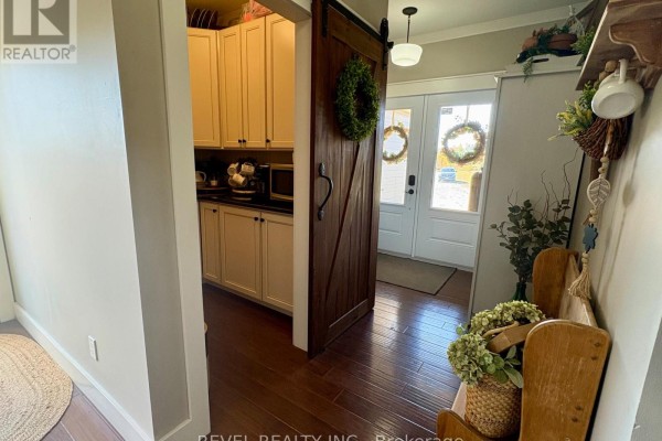View of an open doorway to a kitchen with cream cabinets, and a barn door leading to the front entrance. - 1267 4 & 5 Concession, Cochrane