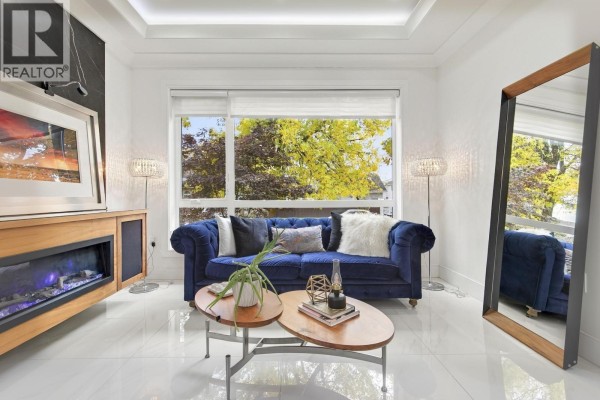 Living room with a navy blue velvet sofa, fireplace, and large window overlooking trees. - 1267 E 53rd Avenue, Vancouver