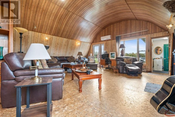 Living room with brown leather furniture, wood-paneled walls, a curved ceiling, and large windows. - 1268 Plains Road, Debert